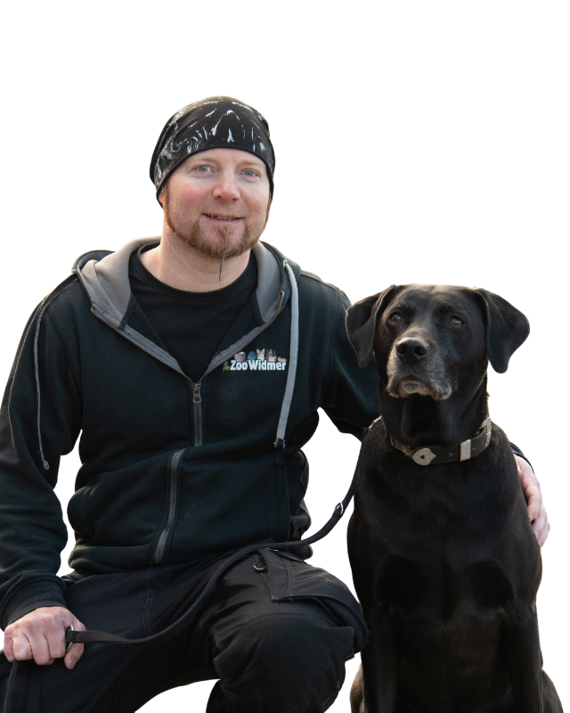 Mann mit schwarzem Hund, beide in neutraler Pose, der Mann trägt ein schwarzes Sweatshirt mit Logo.