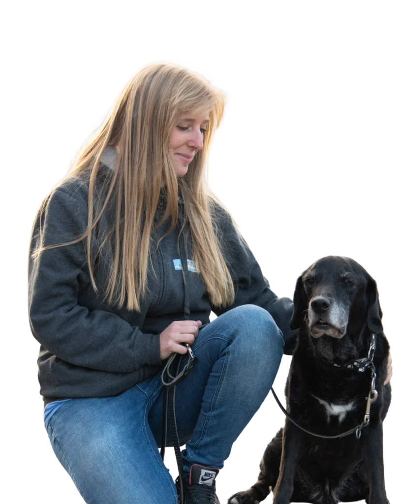 Frau mit langen blonden Haaren, die sich zu einem schwarzen Hund mit Leine hinunterbeugt.